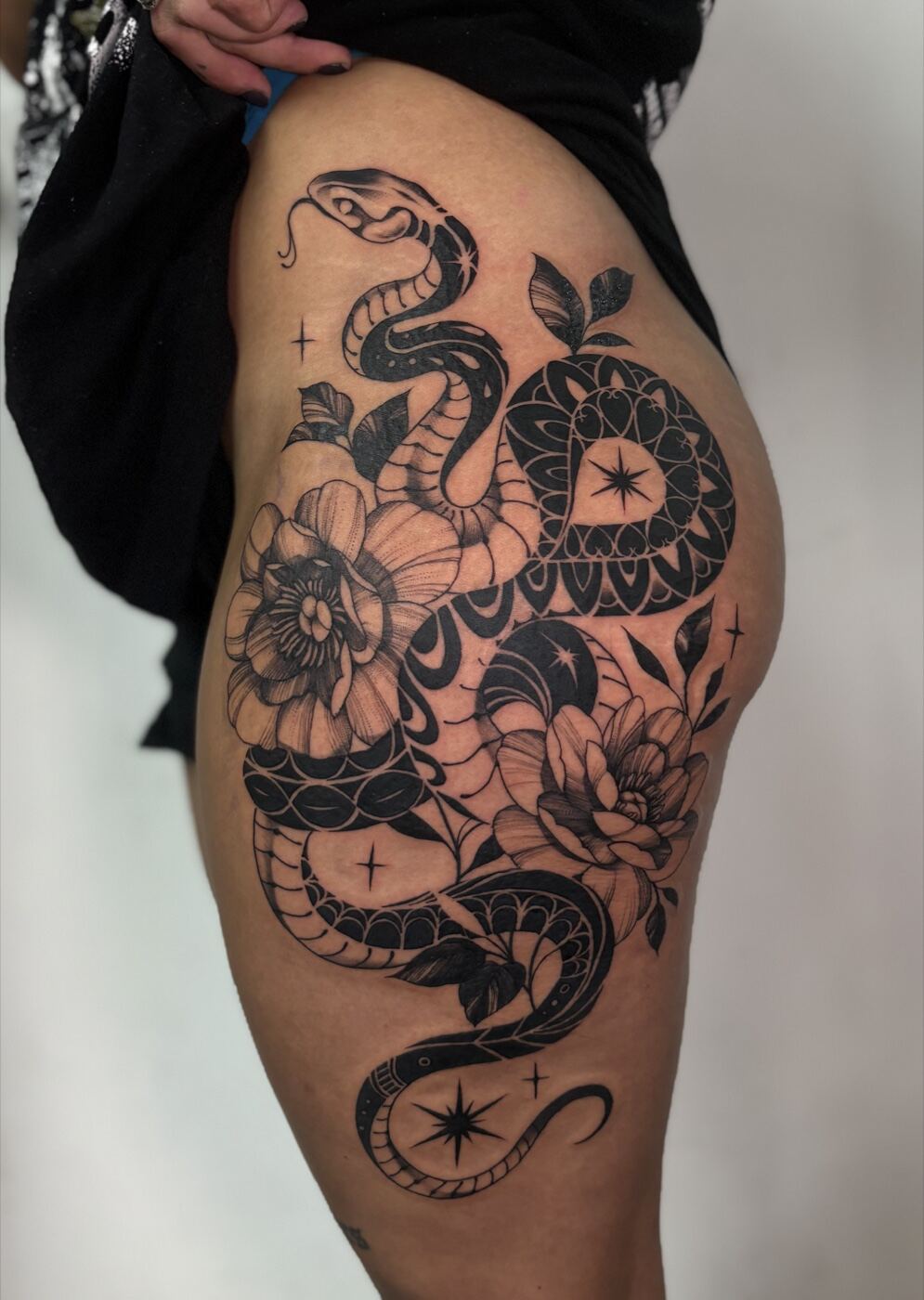 Black and grey illustrative hip piece, snake coiled with florals and stars