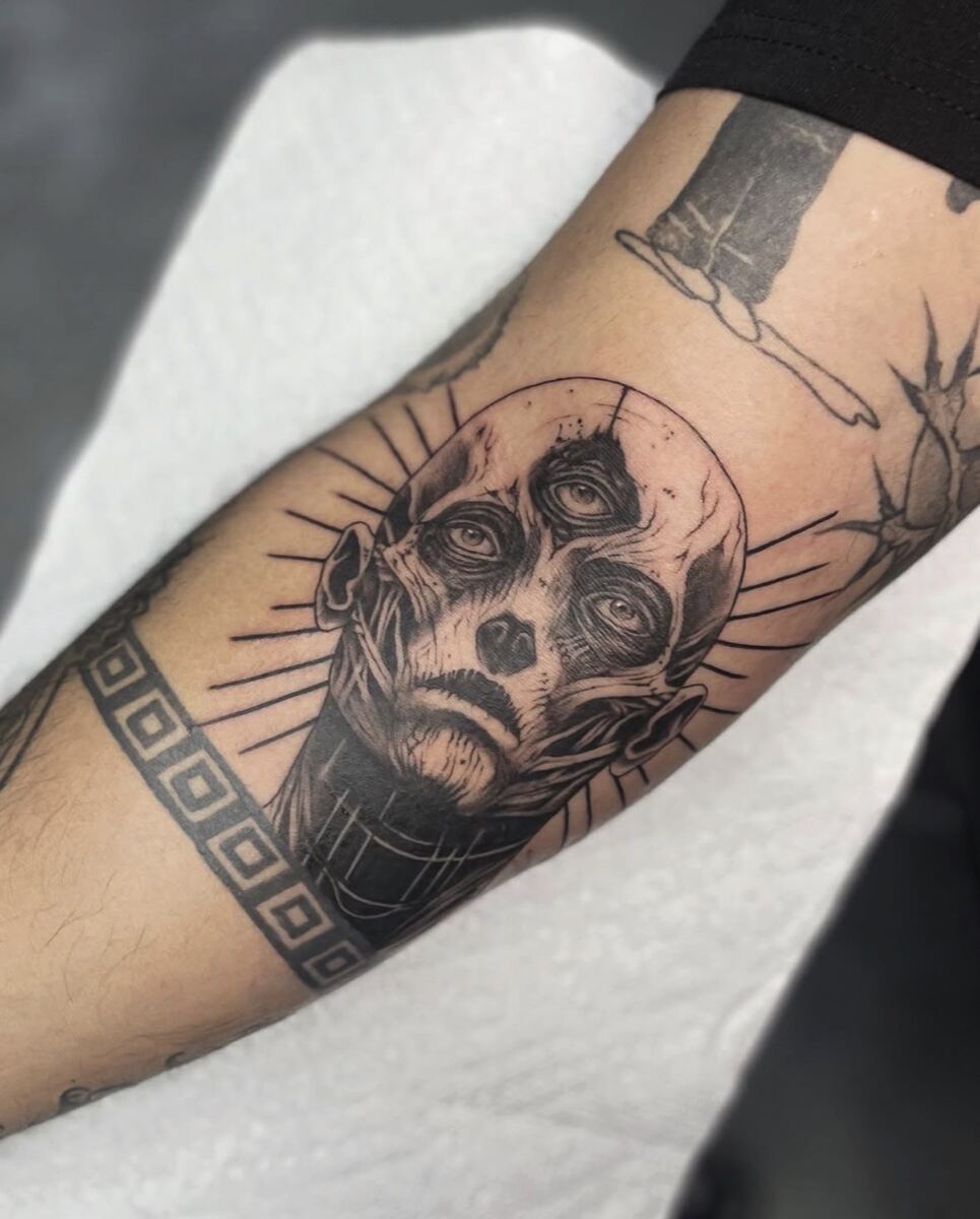 Black and grey illustrative forearm, multi eyed figure with rays